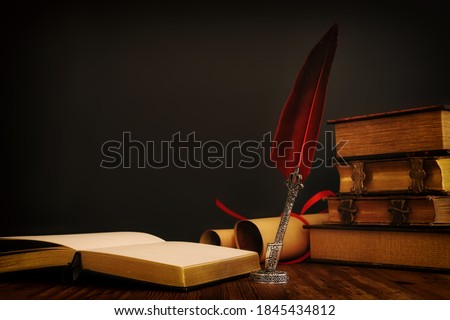 Old feather quill ink pen with inkwell and old books over wooden desk in front of black wall background. Conceptual photo on history, fantasy, education and literature topic. Royalty-Free Stock Photo #1845434812