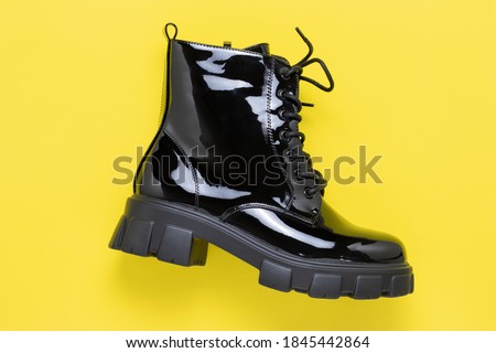 Black short boot on a yellow background. Patent leather shoes. Autumn women's lace-up shoe. Modern outdoor boots on tractor sole. Casual fashion concept.