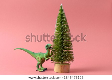 festive minimal greeting card with 
 cute dinosaur and christmas tree on a pink background
