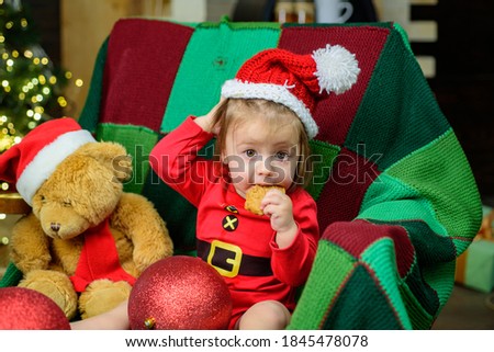 Cute baby face in Santa hat near Christmas tree tasting christmas sweet treats. Happy Childhood, child 1 year old. New year kids