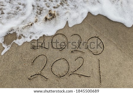 Happy New Year 2021 text on the sea beach. Handwritten inscription 2020 and 2021 on beautiful golden sand beach. Abstract background photo of coming New Year 2021 and leaving year of 2020.