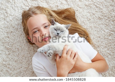 Beautiful little girl lying on the floor with a fluffy cat. A child with an animal. . High quality photo.