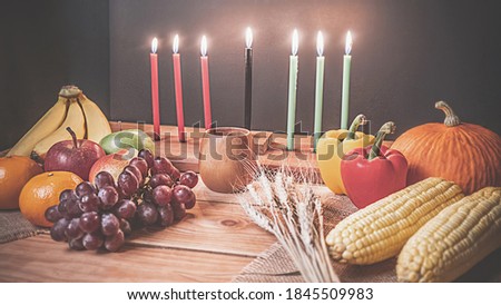 Kwanzaa holiday concept with decorate seven candles red, black and green, gift box, pumpkin,corn and fruit on wooden desk and black background.