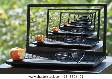 The Droste effect concept: Laptop, apple and eyeglasses on garden table with picture recursively appearing within itself on laptop's monitor Royalty-Free Stock Photo #1845526429