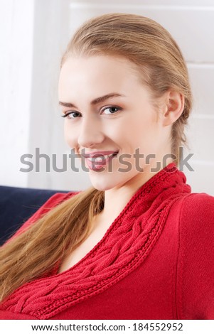 Beautiful caucasian woman sitting ona couch and wearing red pullover. Indoor background.
