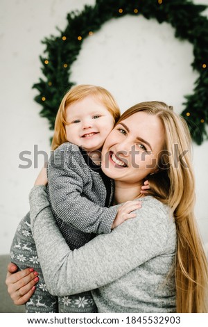 Mother and little child having fun and playing together at home. Portrait loving family close up. Cheerful mom hugging cute baby daughter girl near Christmas tree. Merry Christmas and Happy Holidays.