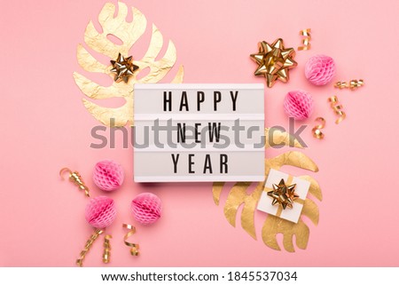 Happy New Year text on white Lightbox with festive gift box, gold and pink decorations, leaves Monstera on amaranth pink paper background. Christmas, new year concept. Flat lay, top view, copy space.