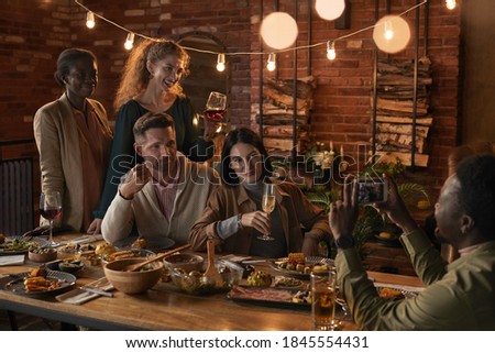 Multi-ethnic group of cheerful adult people taking photo while enjoying party with outdoor lighting
