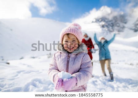 Portrait of cheerful small girl playing in snow in winter nature, playing.