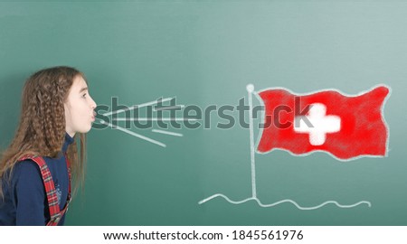 Pre-adolescent girl blowing on the school board drawn on the blackboard Switzerland flag. High resolution photo. Full depth of field. 
