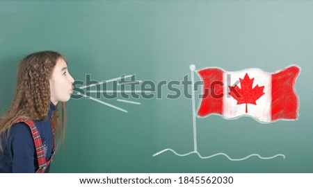 Pre-adolescent girl blowing on the school board drawn on the blackboard Canada flag. High resolution photo. Full depth of field. 