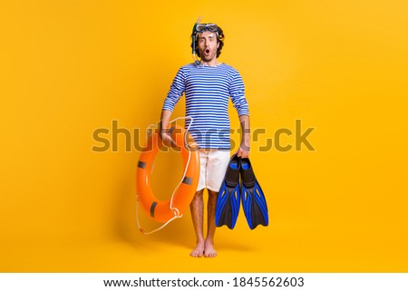 Full length photo of amazed barefoot guy hold life buoy flippers wear scuba mask goggles isolated on yellow color background