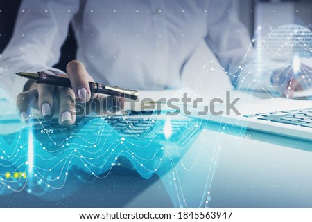 Hands of unrecognizable businesswoman using calculator in blurry office with double exposure of financial graphs. Toned image
