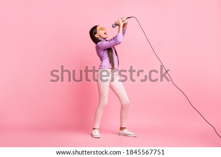 Full size photo of small kid girl sing song on mic wear purple sweater trousers isolated over pastel color background Royalty-Free Stock Photo #1845567751