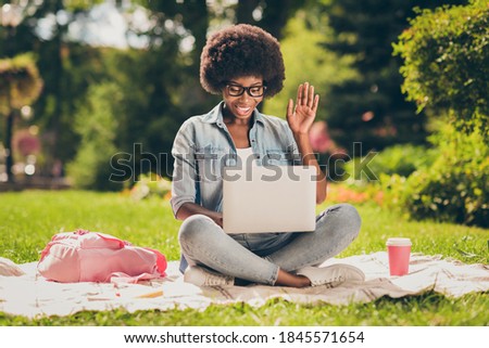 Photo portrait of black skinned girl watching comedy movie laughing loudly with laptop sitting in park wearing glasses