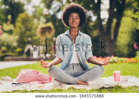 Photo portrait of black skinned young woman sitting in city green park near bag doing yoga asana lotus having pause chill rest closed eyes