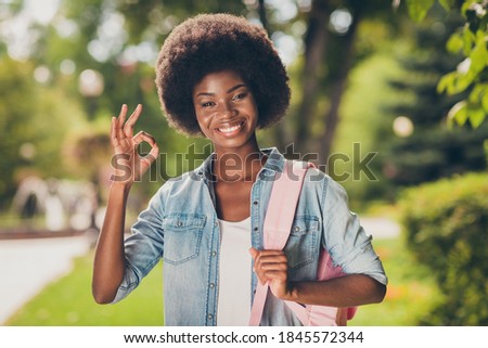 Photo portrait of black skinned girl smiling demonstrating ok gesture good satisfied well done wearing fashionable outlook in city park