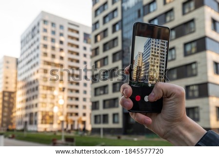 Real estate agent taking a photo of property with his smartphone. Close-up of hands of realtor with the phone taking pictures of new residential building
