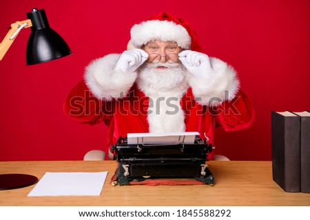 Photo of santa claus grey beard sit table take off eyewear think retro typewriter lamp paper book wear x-mas costume coat cap glasses isolated red color background