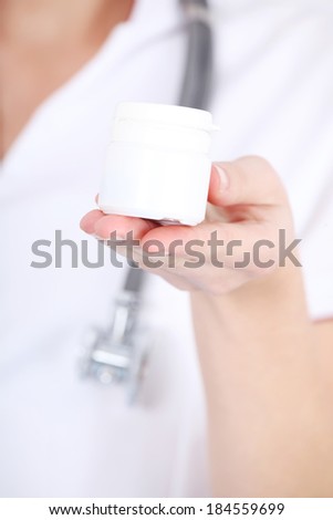 Young woman doctor nurse is holding white empty plastic bottle. Focus on the bottle.