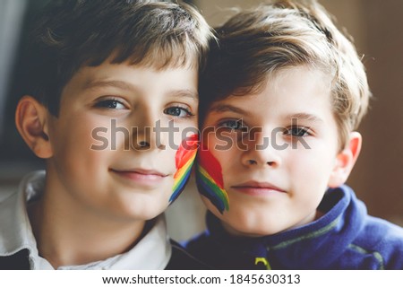 Two kid boys with painted rainbow with colorful colors on face during pandemic coronavirus quarantine. Children make and paint rainbows around the world. Siblings, best friends