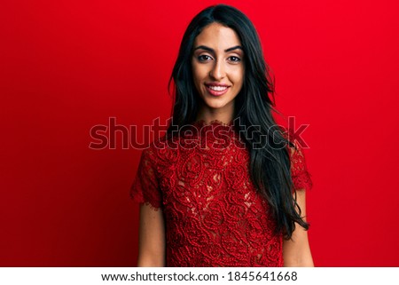 Beautiful hispanic woman wearing elegant clothes over red background looking positive and happy standing and smiling with a confident smile showing teeth 
