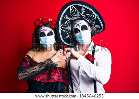 Couple wearing day of the dead costume wearing medical mask smiling in love showing heart symbol and shape with hands. romantic concept. 