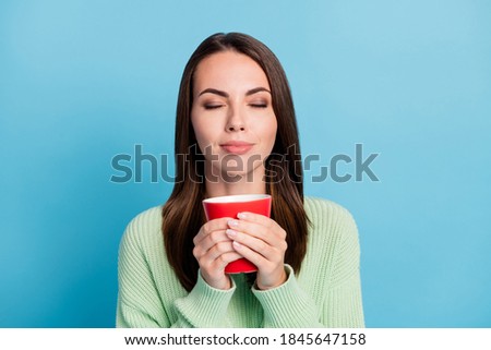Photo portrait of pretty female student smelling hot drink in the red cup holding in hands isolated on bright blue color background