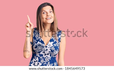 Beautiful caucasian woman wearing summer dress showing and pointing up with finger number one while smiling confident and happy. 
