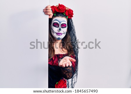 Young woman wearing day of the dead custome holding blank empty banner smiling cheerful offering palm hand giving assistance and acceptance. 