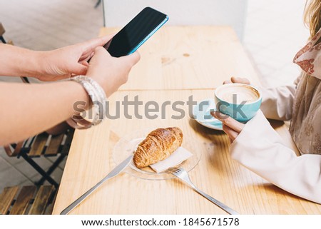 Girl's hands taking a picture of a breakfast while her friend is having a coffee.