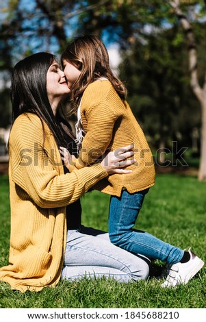 Little cute child baby girl kiss on cheek and hug, embrace with happy pretty woman in green park.