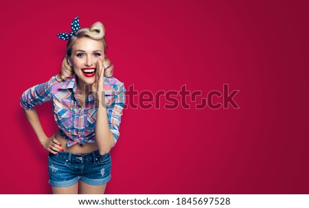 Beautiful happy excited woman holding hand near open mouth. Girl dressed in pin up. Blond model at retro fashion vintage concept. Over red background. Copy space area for sign or text.