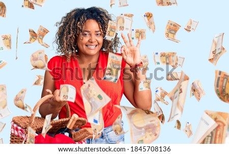 Young african american plus size woman holding picnic wicker basket with bread doing ok sign with fingers, smiling friendly gesturing excellent symbol