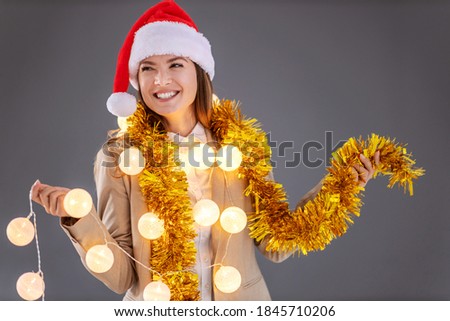 Young smiling businesswoman with santa's hat on the head, with christmas decorations around neck celebrating christmas eve.