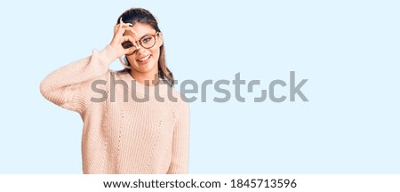 Young beautiful woman wearing casual winter sweater and glasses smiling happy doing ok sign with hand on eye looking through fingers 