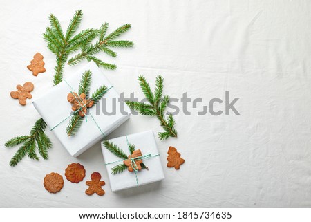 Christmas gifts wrapped in white paper and decorated with spruce sprigs and gingerbread cookies on a fabric background