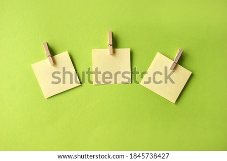 Two yellow sticker with blank space for an inscription or a reminder on a green background, attached to a clothespin. Close-up. Top view.