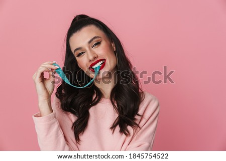 Picture of a young attractive lady standing isolated over pink background stretching bubble gum. Looking at camera