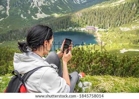 A tourist woman uses a smartphone in the mountains while sitting on the edge of a cliff.