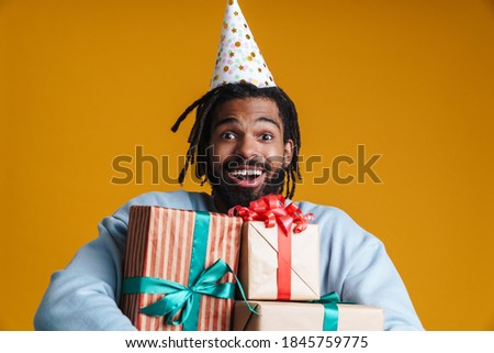 Portrait of an excited young man holding many gifts isolated on yellow background