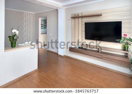 Modern apartment living room with large TV over wooden cabinet Orchid, cork floorboards and door to corridor. Real room of real estate residential house. Royalty-Free Stock Photo #1845763717