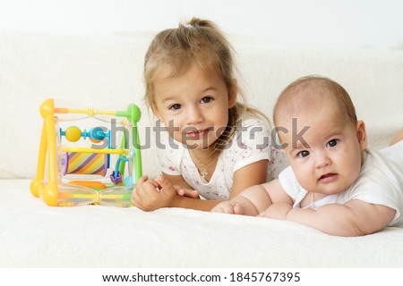 Little smiling kids playing together sitting on the bed. Brother and sister show a newborn a toy. Toddler kids meeting new born sibling.Kids playing and bonding. Children with small age difference