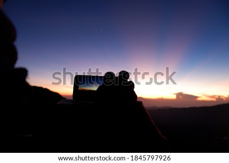 A wonderful scenery of a sunrise on the top of the mountain, a tourist is taking a picture of the sunrise with his phone