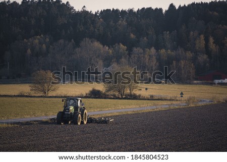 Green tractor ploughing a dry dusty field on the countryside in the spring sunset