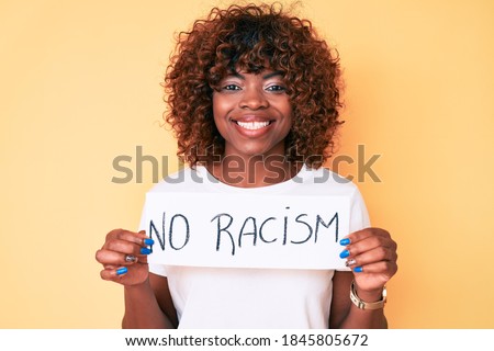 Young african american woman holding no racism banner looking positive and happy standing and smiling with a confident smile showing teeth  Royalty-Free Stock Photo #1845805672