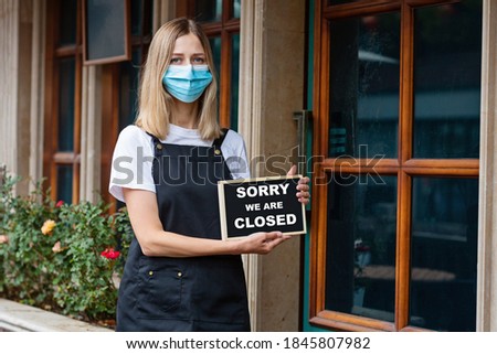 Caucasian waitress woman wearing medical mask holds SORRY WE'RE CLOSED. Coronavirus pandemic. Government shutdown of restaurants, shopping stores, non essential services