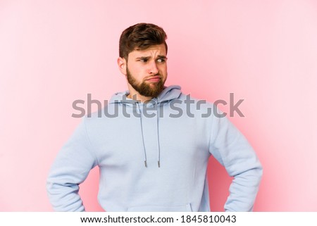 Young caucasian man isolated on pink background confused, feels doubtful and unsure.