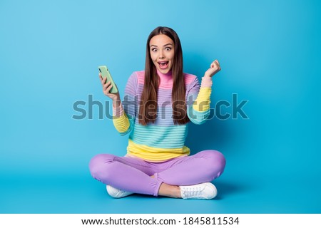 Portrait of glad cheerful girl sitting lotus position crossed legs using gadget browsing media isolated on bright blue color background