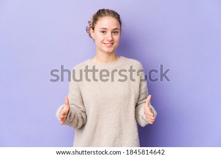 Young caucasian woman on purple background holding something with both hands, product presentation.